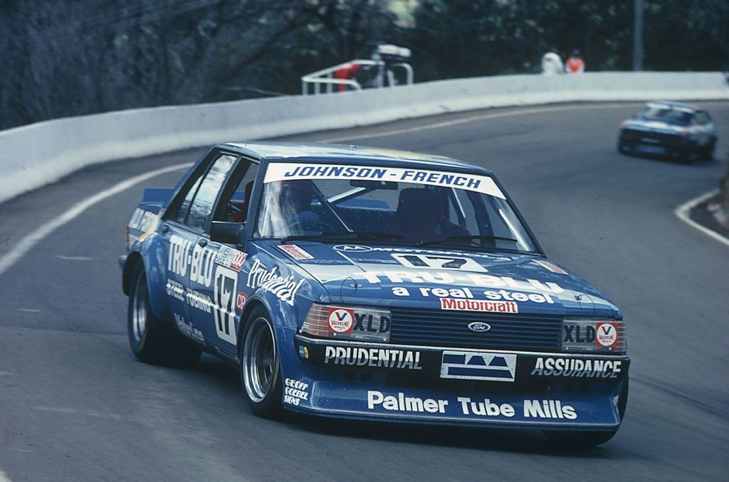 Un coche de carreras azul, modelo Ford, compitiendo en una pista. Tiene varios patrocinadores en su carrocería, incluyendo 'Johnson-French' y 'Prudential'.